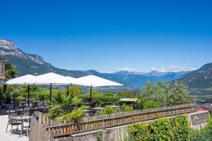 a patio with tables and umbrellas with mountains in the background at Hotel Sigmundskron in Appiano sulla Strada del Vino