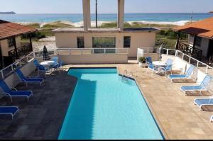 una piscina con sillas y el océano en el fondo en Praia das Dunas Residence Club, en Cabo Frío