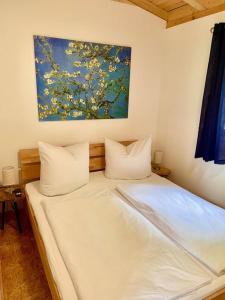 a bed with white sheets and a painting on the wall at Ferienhaus Bachrauschen in Schöna