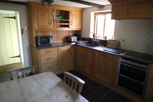 cocina con armarios de madera, mesa y microondas en Medieval Cottage in rural Monmouthshire. en Raglan