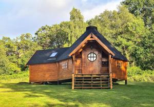 a wooden cabin with a black roof on a grass field at Seal Point Cabin - Luxury Glamping in Cairndow