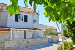 a white house with green shutters and a stone wall at Apartman Paula in Milna