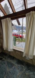 a window with white curtains and a red car at Puerto La Casa in San Martín de los Andes