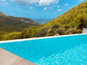 une piscine bleue avec une montagne en arrière-plan dans l'établissement DOMAINE DE MAPOU, à Les Anses-d'Arlet