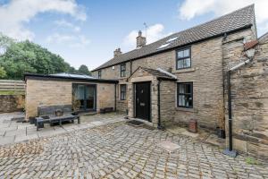 una antigua casa de piedra con un patio de ladrillo en Carr House Farm en Glossop