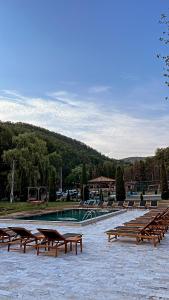 a pool with wooden benches and a row of tables at Pensiunea Valea Gepisului in Groşi