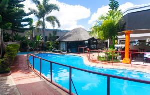 a pool at a resort with palm trees and a building at Nomads Court Chudleigh in Lusaka