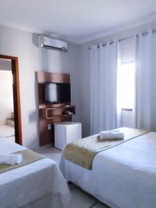 a hotel room with two beds and a flat screen tv at Hotel Cantinho Verde in Teixeira de Freitas