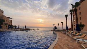 Comfy Stays Sea View Apartments at DeadSea Samarah Resort في السويمة: مسبح مع كراسي و المحيط وقت الغروب
