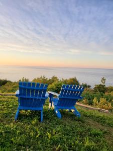 dos sillas azules sentadas en la hierba cerca del océano en Motel du Cap St-Yvon, en Cloridorme