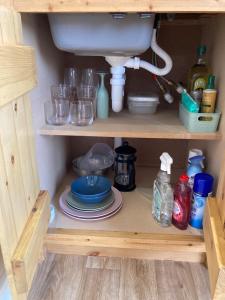 a kitchen cabinet with a sink and plates and glasses at Delor - Bryntalch Glamping Pods in Montgomery