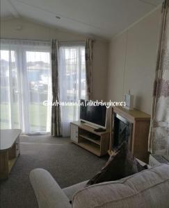a living room with a couch and a tv and windows at Hakuna Matata Holiday Homes - Newquay Bay Resort in Newquay