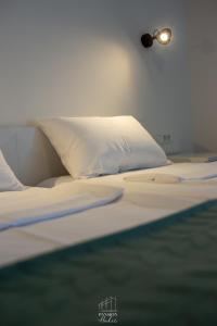 a bed with white sheets and a light on the wall at Pansion Hukić B&B in Tuzla