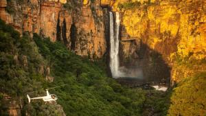 a helicopter is flying over a waterfall at Cooinda Lodge Kakadu in Jabiru