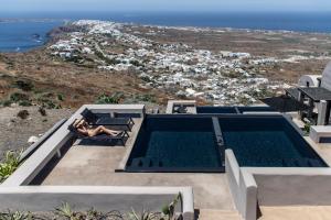 a person sitting in a chair next to a swimming pool at Nimbus Santorini in Oia