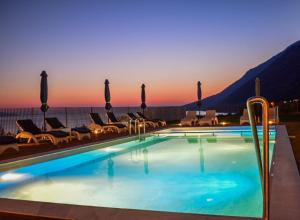 a swimming pool with chairs and a sunset in the background at Pantheon Hotel & Suites in Nerotriviá