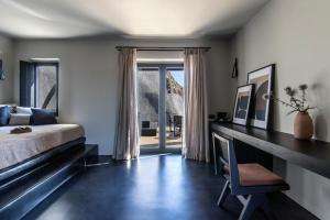 1 dormitorio con cama y escritorio con ventana en Nimbus Santorini, en Oia