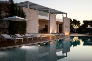 a house with a swimming pool with chairs and an umbrella at Montegrottone Resort & Spa in Polignano a Mare
