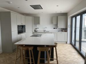 a kitchen with white cabinets and a island with bar stools at Galwad y Mor - Balcony, Sea View, Short walk to beach & several eateries in Haverfordwest