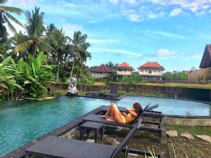 una mujer tumbada en un banco junto a una piscina en Ubud Rice Field House, en Ubud