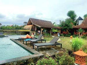 a woman sitting on chairs next to a swimming pool at Ubud Rice Field House in Ubud