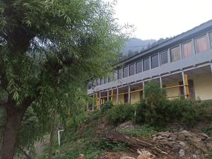 a building on a hill next to a tree at Midway Home stay in Jibhi