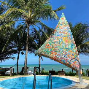 ein Pool mit einem bunten Regenschirm neben Palmen in der Unterkunft As Coloridas in Praia dos Carneiros