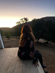 a woman sitting on a wooden deck watching the sunset at Árbol de la Vida Glamping Valle de Guadalupe 