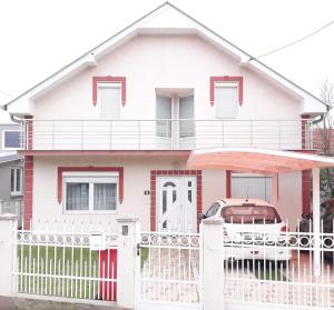 a pink house with a white fence and a car at Pansion Eden in Niš