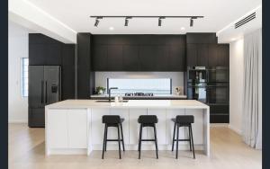 a kitchen with black cabinets and a white island with bar stools at Central Coast - Luxurious Beach House 400m to Beach in Bateau Bay