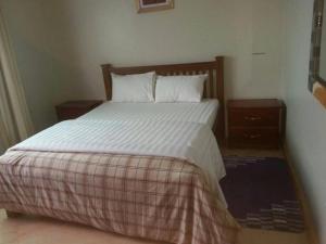 uma cama com lençóis brancos e almofadas num quarto em The Greenville Home em Mbarara