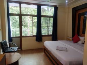 Hotel Amandeep في دارامشالا: غرفة نوم بسرير ومكتب ونافذة