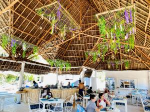 a restaurant with tables and chairs under a straw roof at Badolina Bungalows in Nungwi