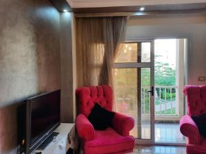 a living room with two red chairs and a television at Lovely 2-bedrooms Apartment with Garden view in Madinaty in Cairo