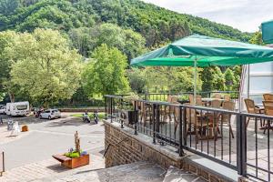 a patio with a green umbrella and chairs and a parking lot at Hotel Le Postillon in Esch-sur-Sûre