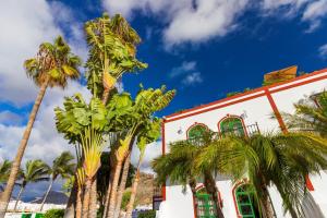 a white building with green windows and palm trees at First Line Luxury Apartment by El Sirocco in Puerto de Mogán