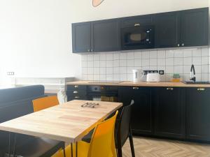 une cuisine avec des armoires noires et une table en bois avec des chaises jaunes dans l'établissement Pau's Appart - Pau Centre, à Pau