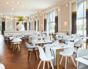un restaurant avec des tables blanches et des chaises blanches dans l'établissement Hôtel Cosmos & Spa, à Contrexéville