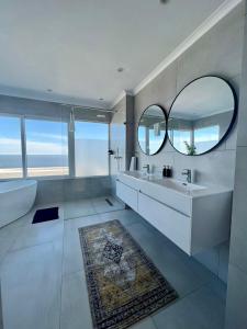 a bathroom with a large mirror and a tub and a sink at Bay Reflections Camps Bay Luxury Serviced Apartments in Cape Town