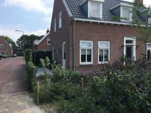 a brick house with white windows and purple flowers at De Logeerkamer Gapinge in Gapinge