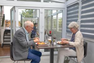 un hombre mayor y una mujer sentados en una mesa comiendo comida en Gardermoen Hotel Bed & Breakfast, en Gardermoen