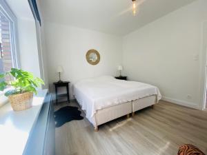 a white bedroom with a bed and a clock on the wall at Lovely, renovated appartment, near the beach. in De Haan