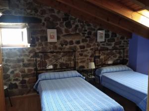 2 camas en una habitación con una pared de piedra en Casa Rural La Barcenilla en Herada