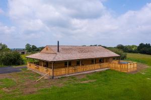 ein großes Holzhaus mit einem Dach auf einem Feld in der Unterkunft Luxury Log Cabin with a Hot Tub in Stone