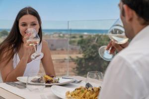 uma mulher sentada à mesa com um homem a beber vinho em Perla Saracena Hotel & Restaurant em Salve