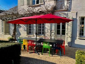 une table avec des chaises colorées et un parapluie rouge dans l'établissement Les gîtes du Champ-De-Bataille, à Sainte-Opportune-du-Bosc