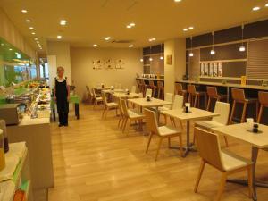 a woman standing in a restaurant with tables and chairs at Hotel Green With in Sendai