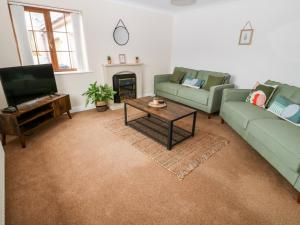 a living room with two green couches and a television at Yr Hen Efail in Cemaes Bay