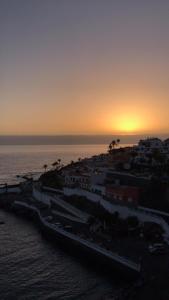 een zonsondergang boven een stad en de oceaan met gebouwen bij Apartamento Playa Chica in Puerto de Santiago