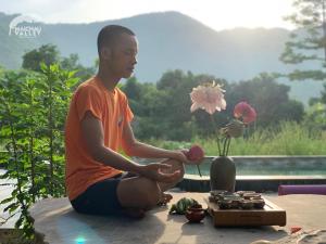 a young man sitting on a table with a vase of flowers at Mai Chau Valley Retreat in Mai Chau